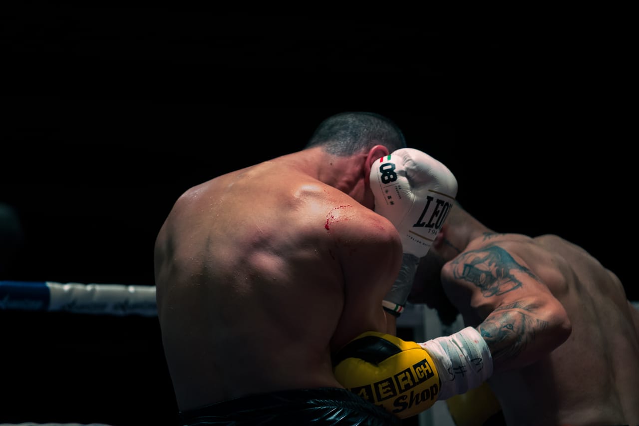 Zwei Boxer im Clinch vor schwarzem Hintergrund, einer mit weissem und einer mit gelbem Handschuh.